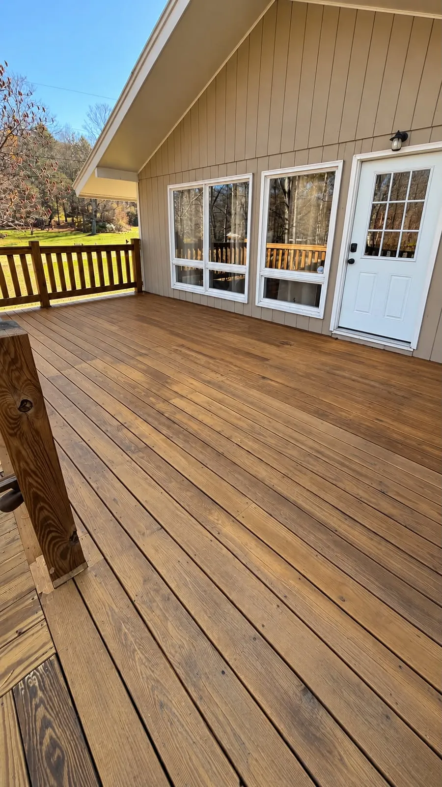 Finished golden wood deck beside a taupe home with white windows