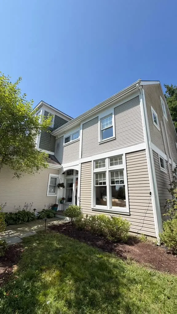 Taupe house siding with crisp white window trim and a landscaped garden